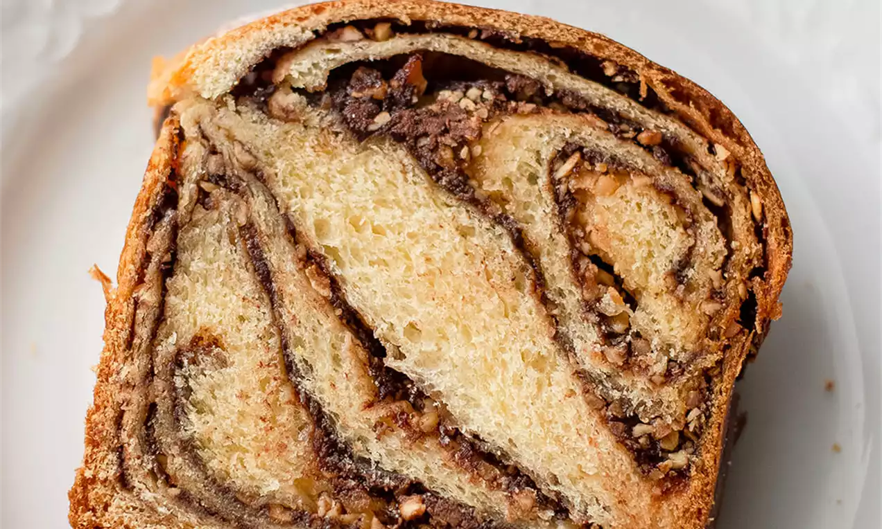 Kriška pletenice s Nutelom i lješnjacima, zlatnosmeđe korice i prozračne unutrašnjosti s tamnim spiralama kreme i komadićima orašastih plodova na bijelom tanjiru