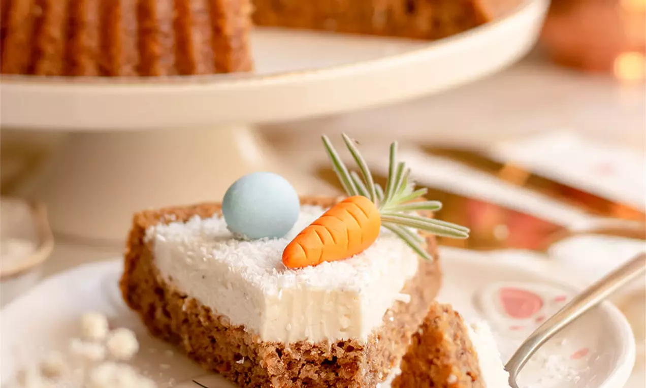 Kremasta kriška torte od smeđeg biskvita s bijelim slojem kreme, ukrašena šarenim fondant jajetom, mrkvicom i ružmarinom na tanjiru